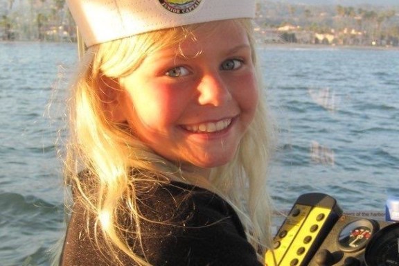 a woman wearing a hat and sunglasses in front of a body of water